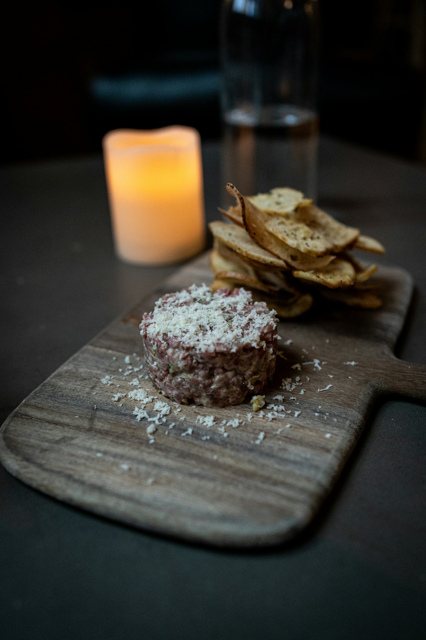 A candlelit plate of tartare on a wooden board, with toasted bread and a blurred candle behind it.