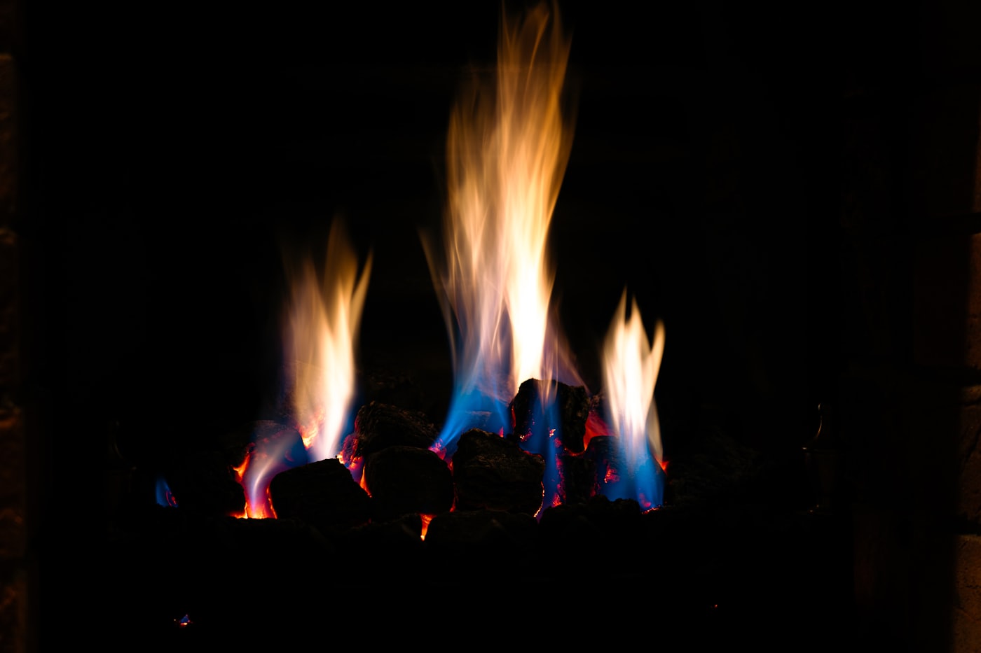 Close flames rising from dark coals, the only light in an otherwise black frame.