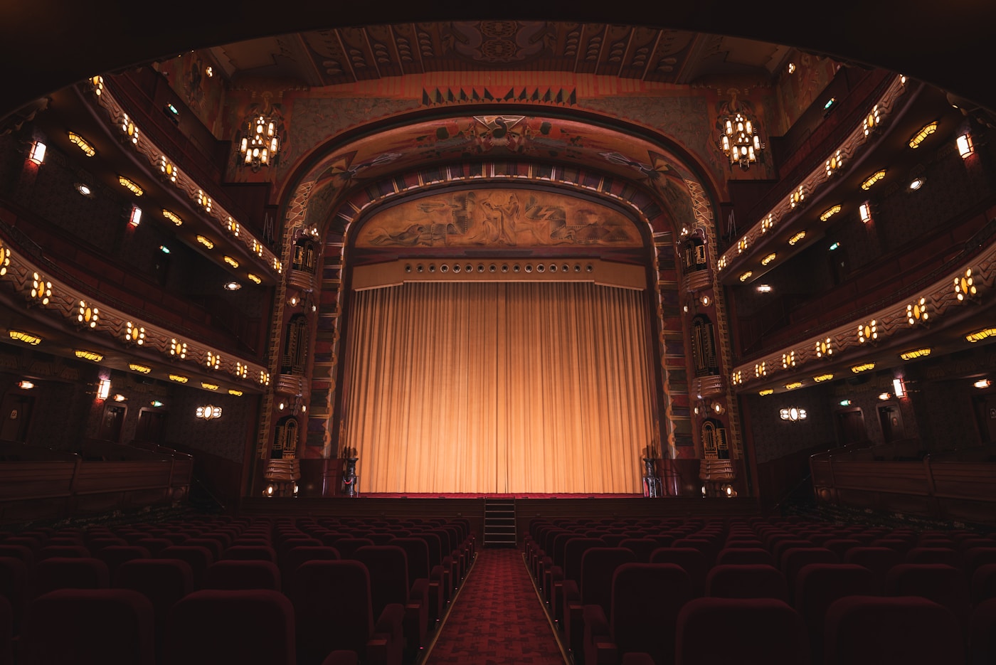 A dark auditorium seen from the rear aisle, seats facing a closed curtain.