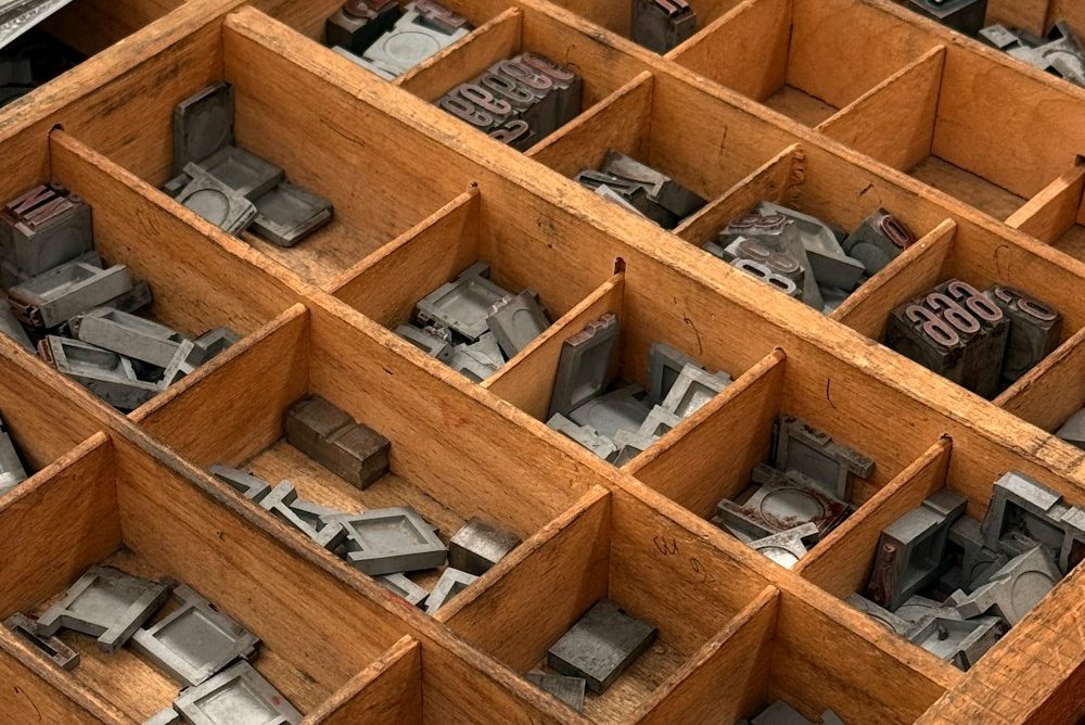 A wooden letterpress case holding scattered metal type.