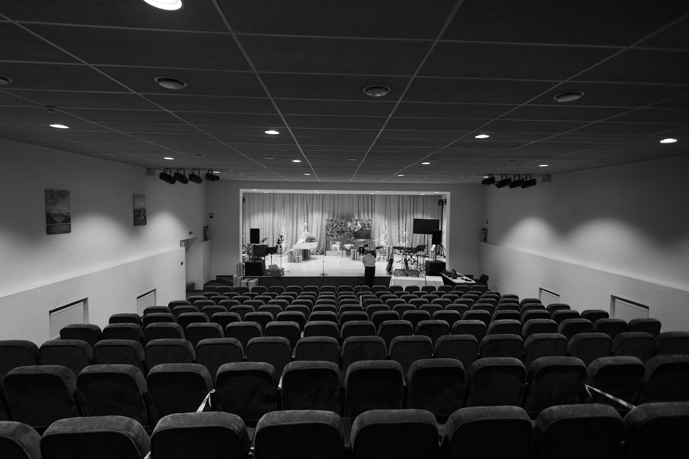 An empty small auditorium, rows of dark seats facing a lit stage.