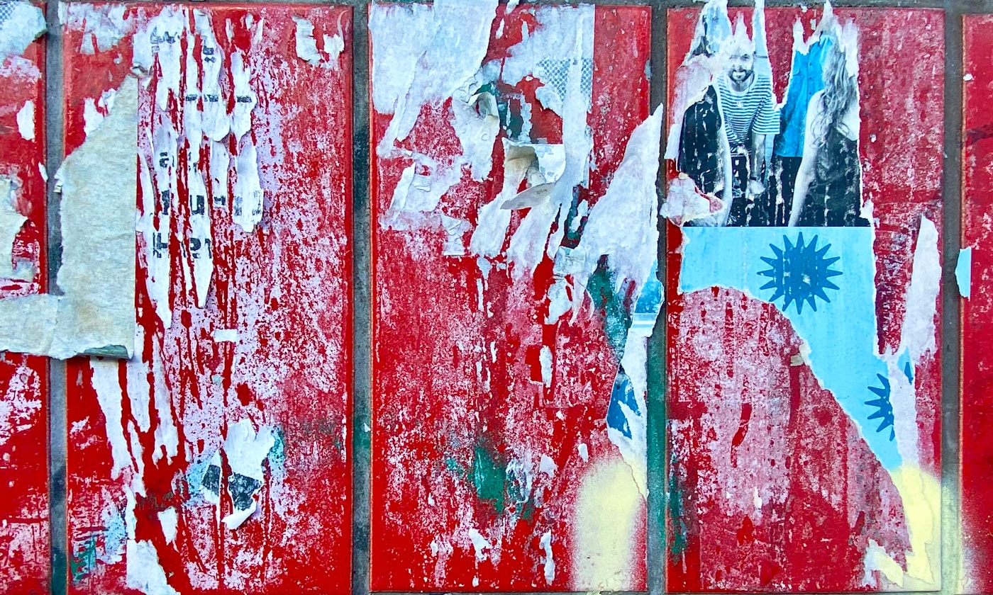 Torn vermilion posters layered on a weathered urban wall.