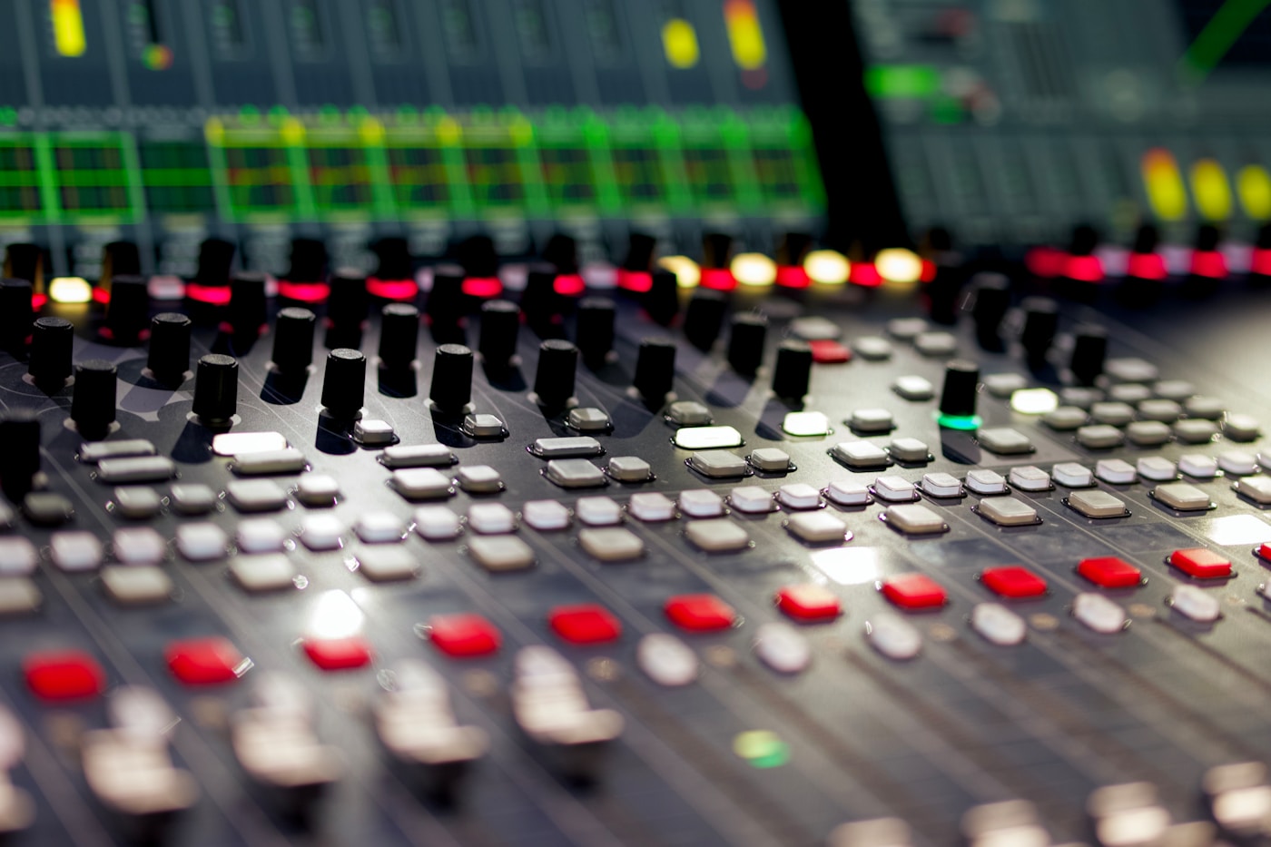 Close view of a dark mixing console with illuminated buttons, red keys, and out-of-focus meter lights.